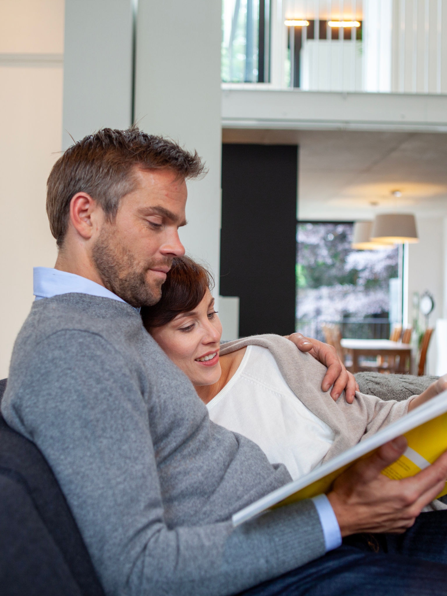 Pareja acurrucada y relajada en su sofá mientras lee un libro a una temperatura perfecta