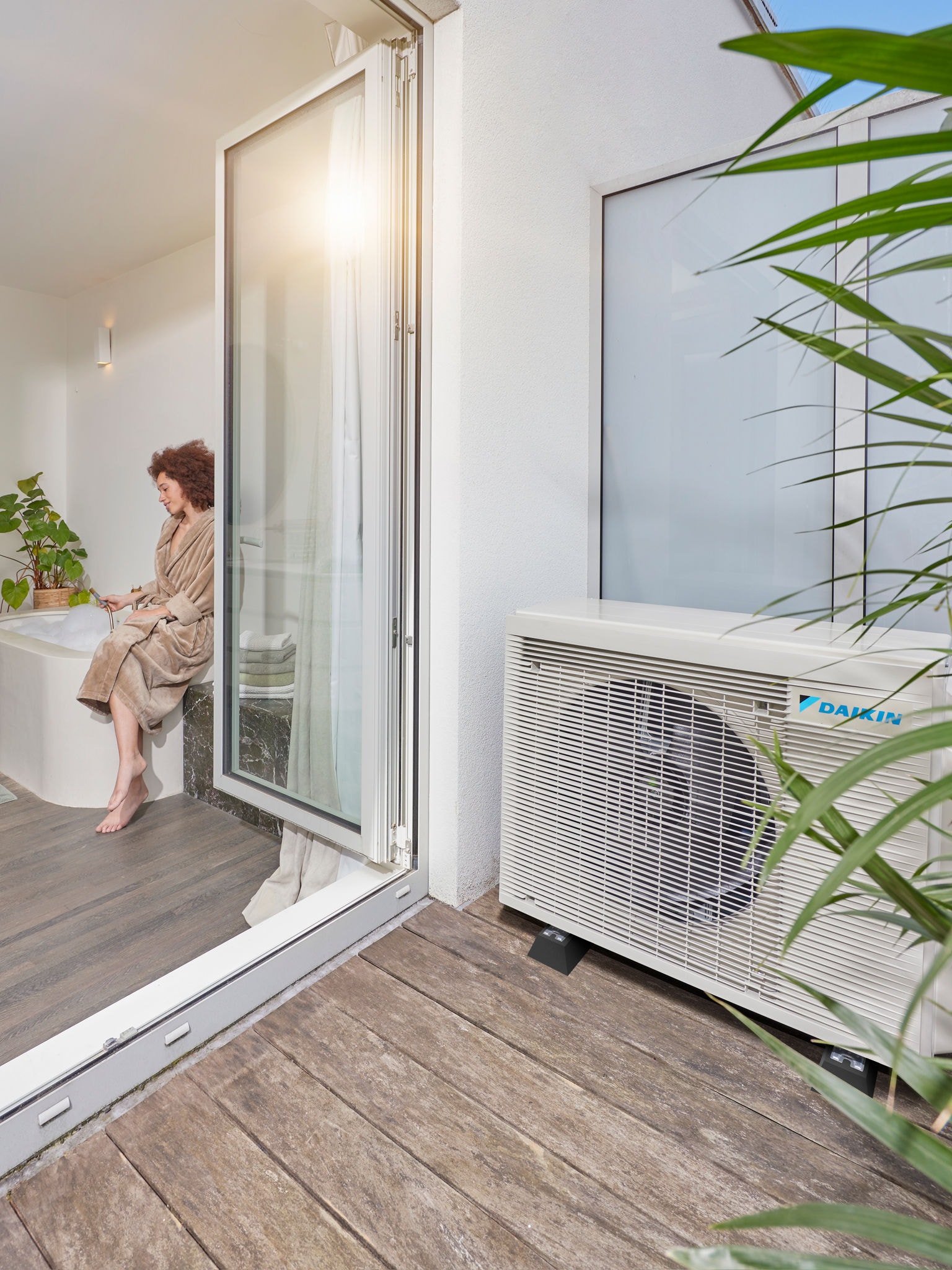 Equipo de aerotermia instalado junto a la terraza, con las puertas abiertas que dan a un cuarto de baño moderno