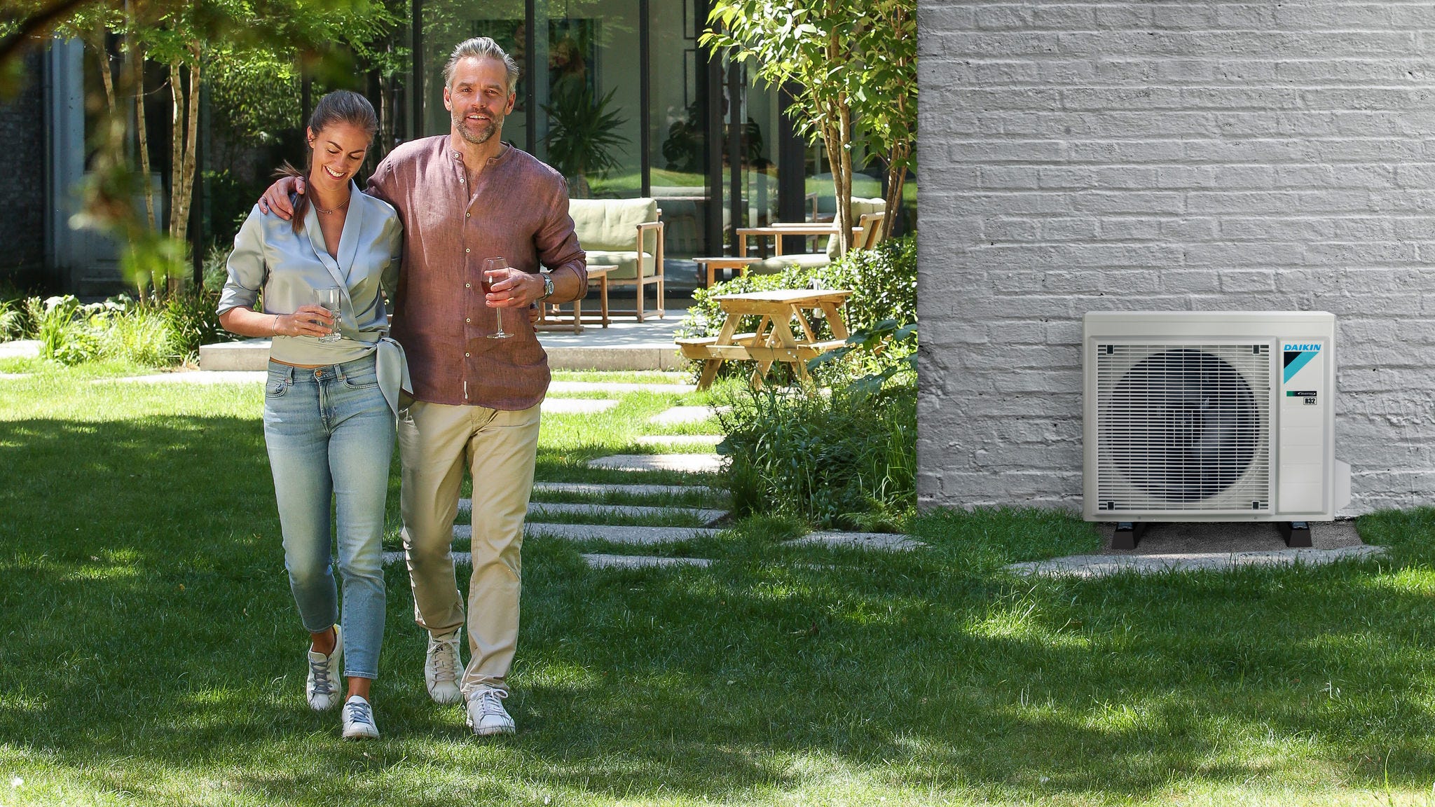 Pareja paseando por el jardín de su casa en el que se ve instalada una unidad exterior de aire acondicionado