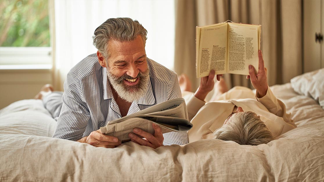 Hombre y mujer leyendo periódico tumbados en la cama