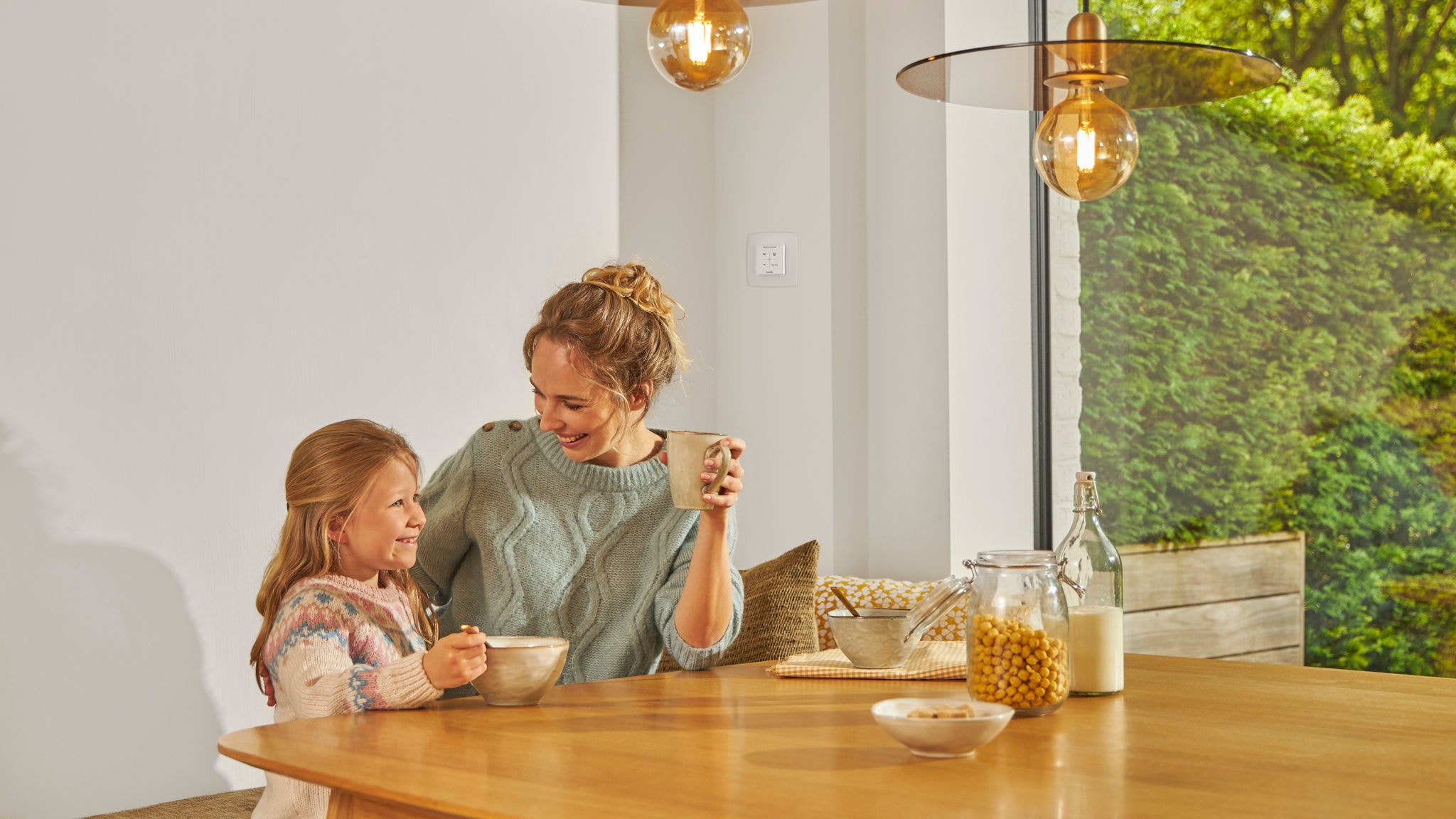 Mujer e hija desayunando y disfrutando de la facilidad de uso de los mandos a distancia inteligentes de ventilación con control de CO2 y humedad
