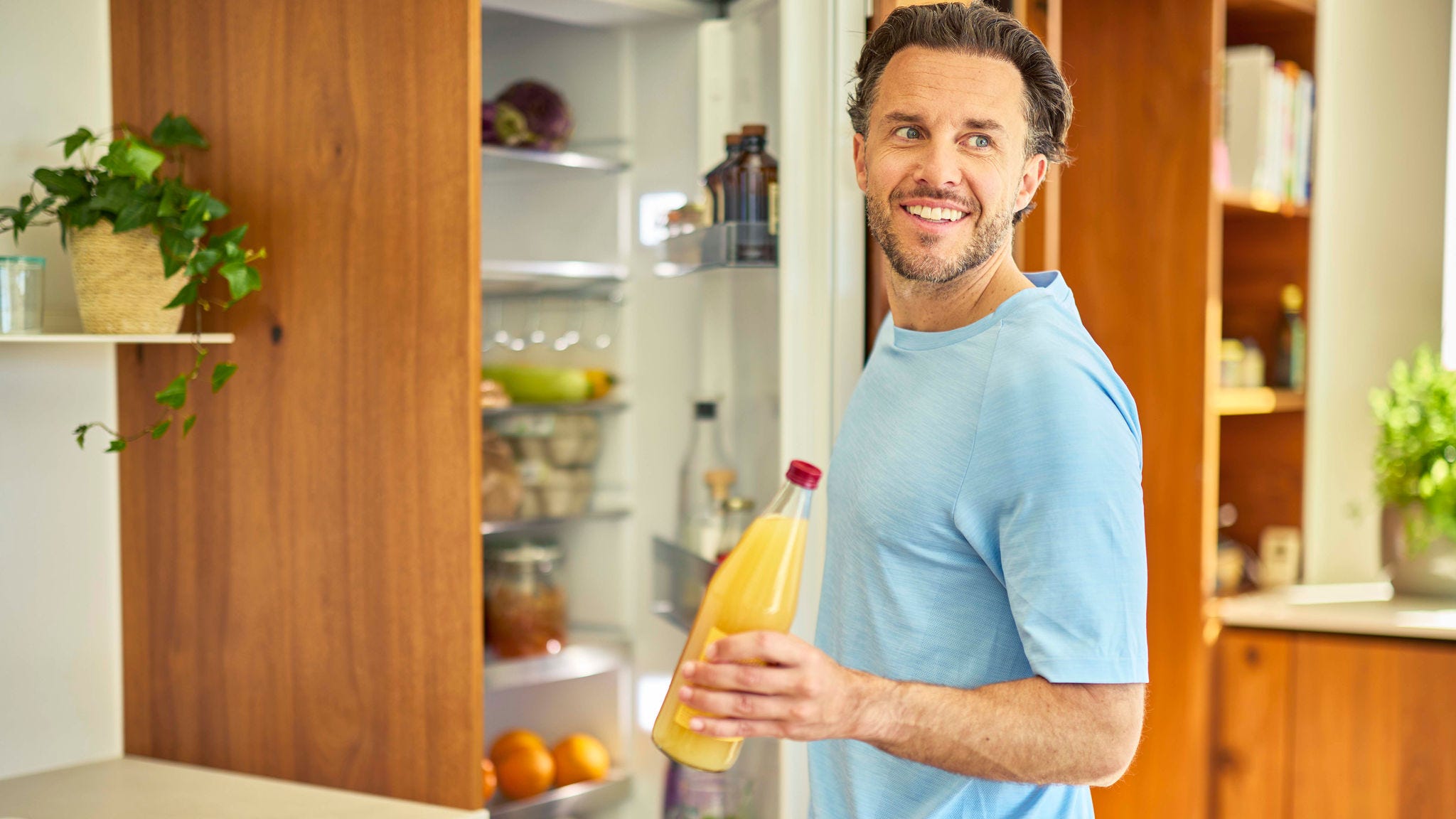 Un hombre sacando una botella de zumo de naranja del frigorífico en una cocina moderna