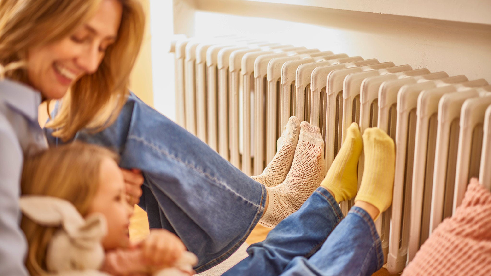 Una madre y su hija calentándose los pies junto a un radiador en una casa cálida y acogedora