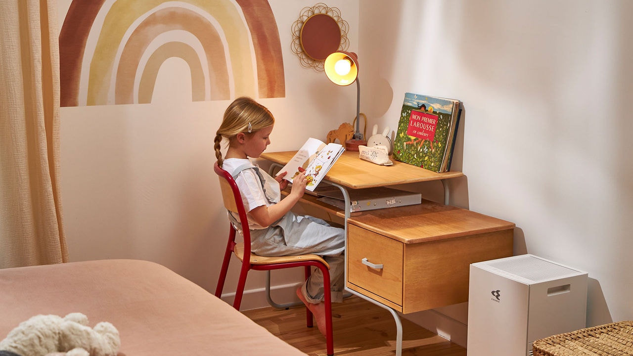 Niña leyendo un libro en el escritorio de su habitación junto a un purificador de aire