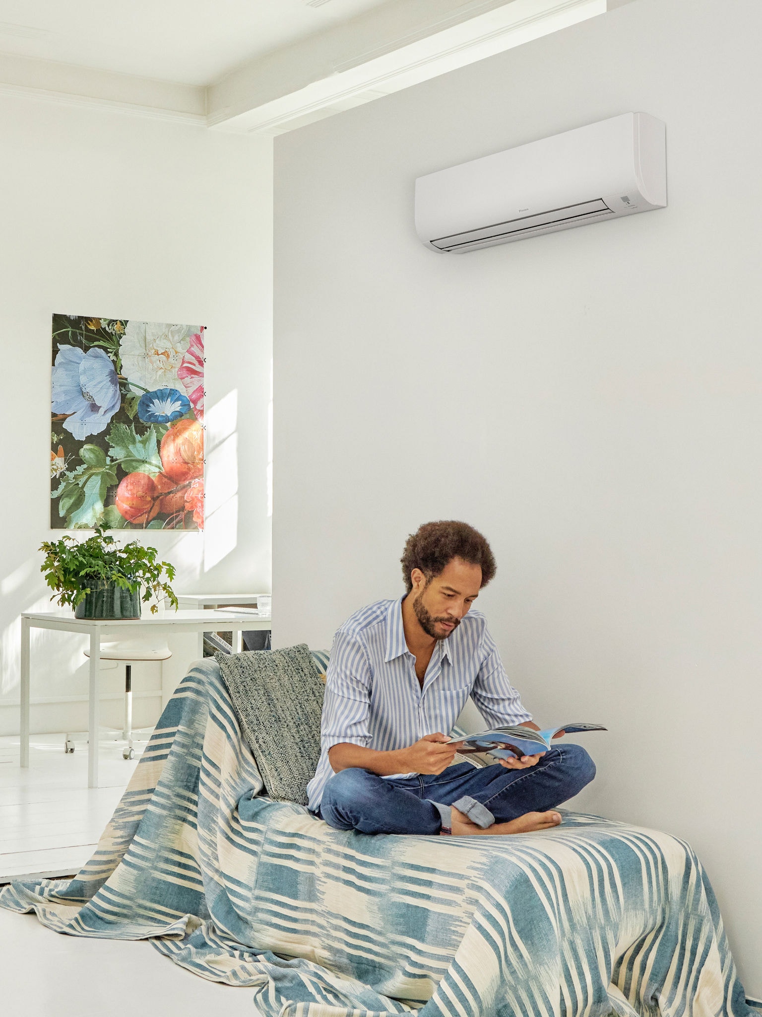 Un hombre leyendo en un salón moderno y luminoso con un equipo de aerotermia instalado en la pared, que ilustra el confort y la eficiencia energética de la tecnología de aerotermia, respaldada por los planes de incentivos del Gobierno