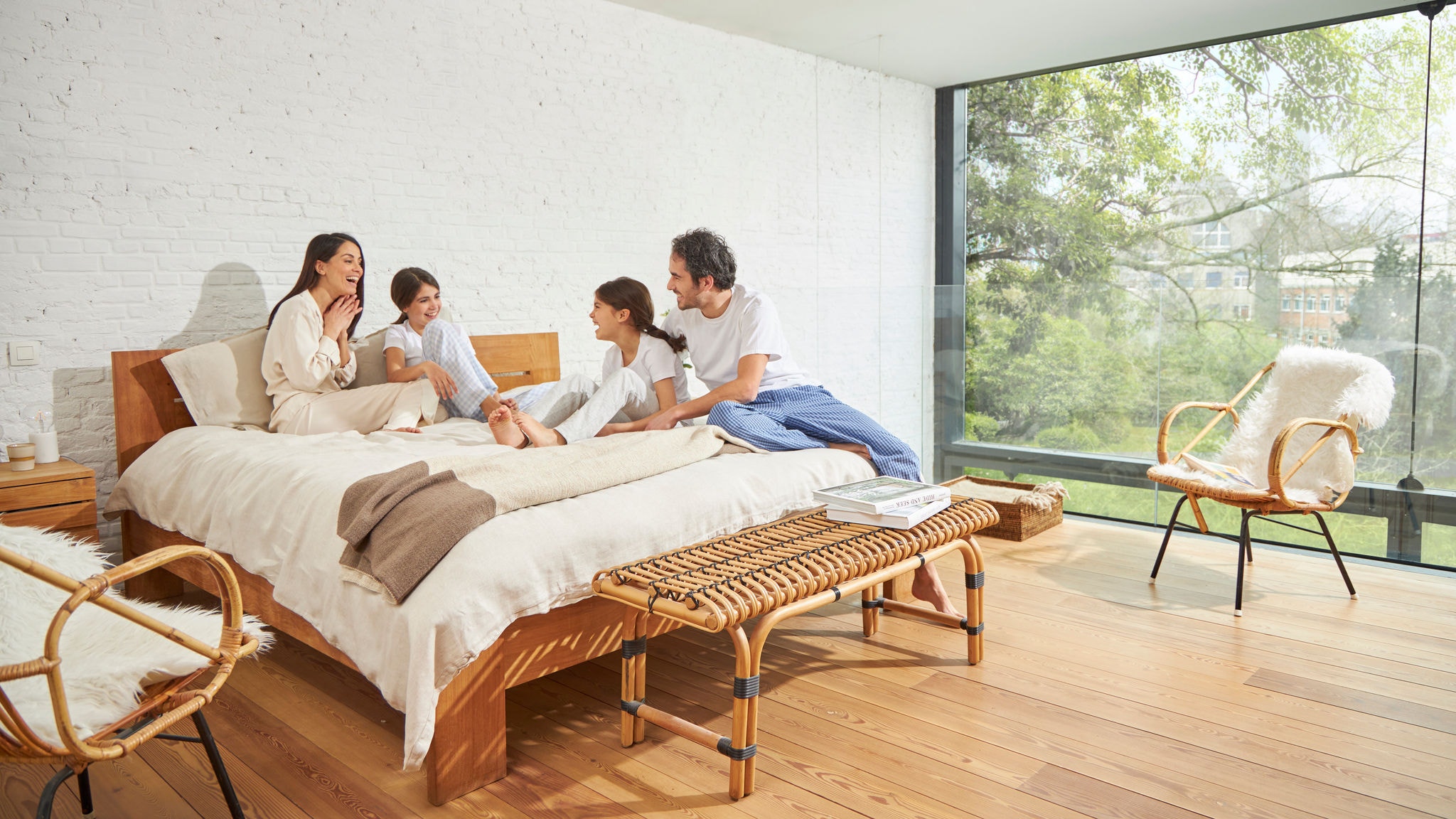 Una familia charlando en la cama de un dormitorio con una gran pared acristalada, buena calidad del aire interior y mucha luz natural
