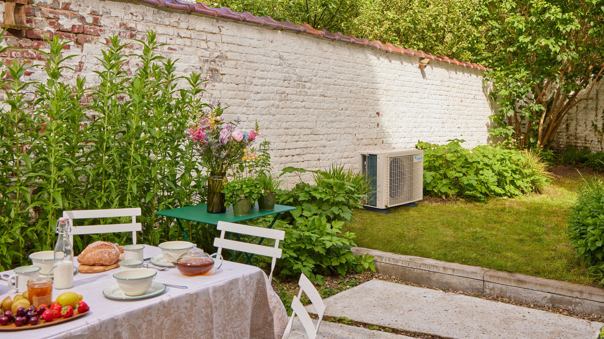 Mesa de desayuno en el jardín con un aire acondicionado inverter que refresca la casa cercana