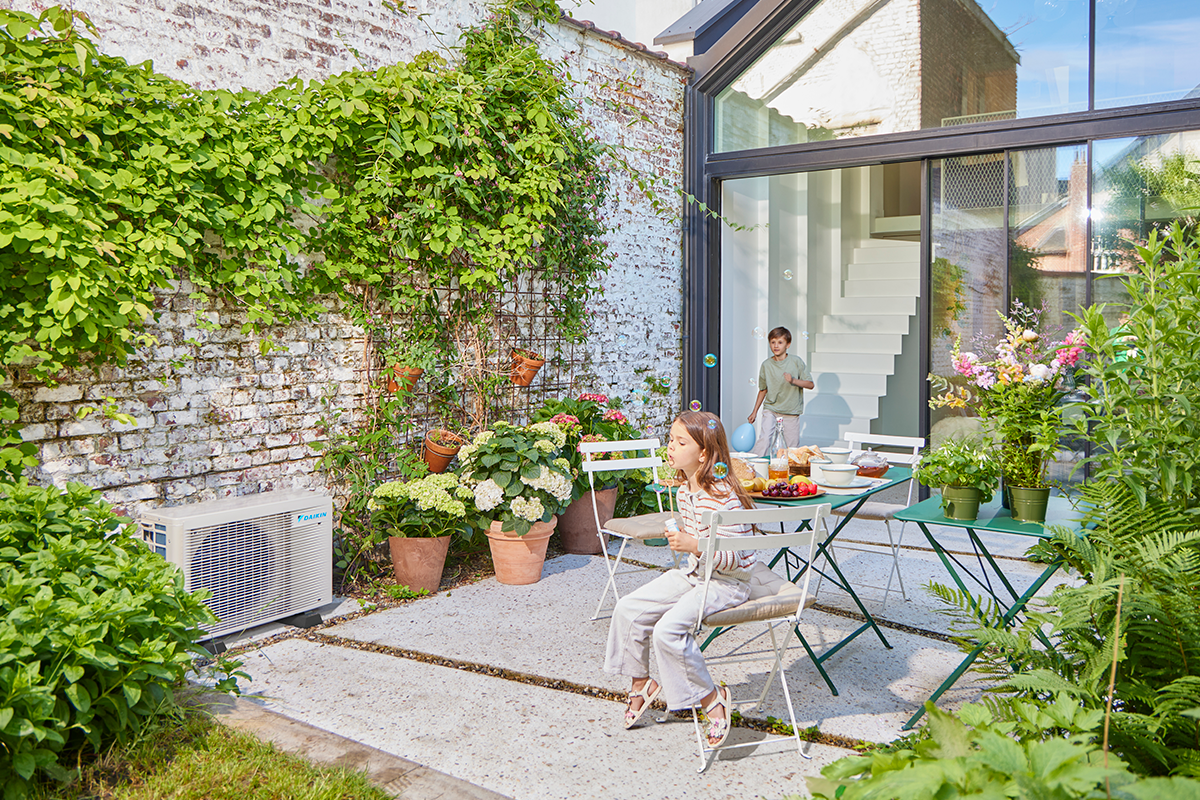 Niños jugando a las canicas en la terraza de un jardín junto a un equipo de aerotermia exterior
