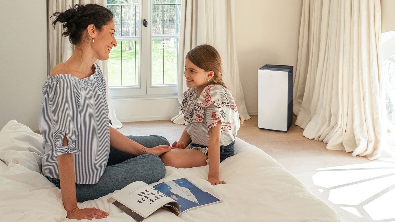 Madre e hija leyendo un libro en la cama de su habitación junto a un purificador de aire