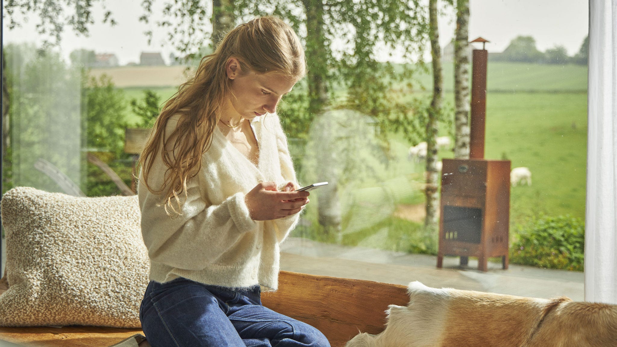 Woman looking at her cell phone by the window of her home